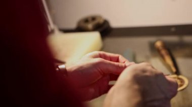 Deri atölyesi. Bir adam küçük bir kemer ilmiği dikiyor.