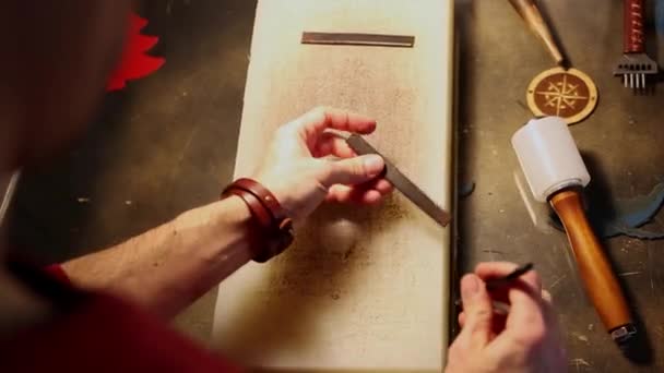 Taller de cuero: un hombre hace agujeros en una pequeña pieza de cuero — Vídeos de Stock