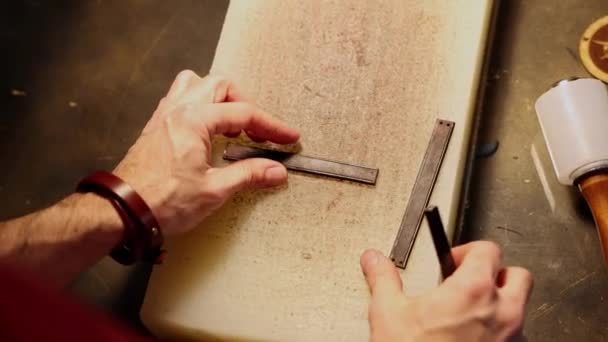 Kožená dílna - muž dělá díry v malém dekorativním kousku kůže — Stock video