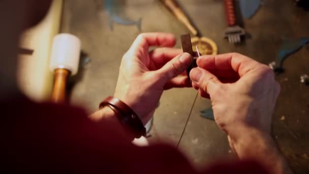 Taller de cuero - un hombre cose una pequeña pieza decorativa de cuero para un cinturón — Vídeos de Stock