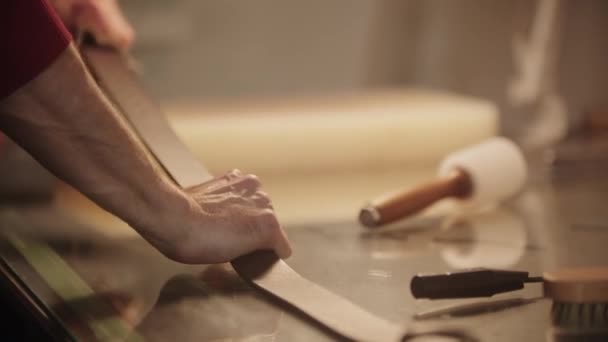 A man stretches a finished leather belt on a table in his hands — Stock Video