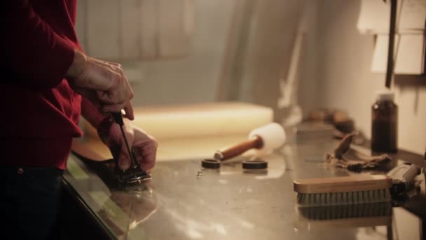 Ein Mann schraubt in einer Werkstatt an einem Ledergürtel am Tisch — Stockvideo