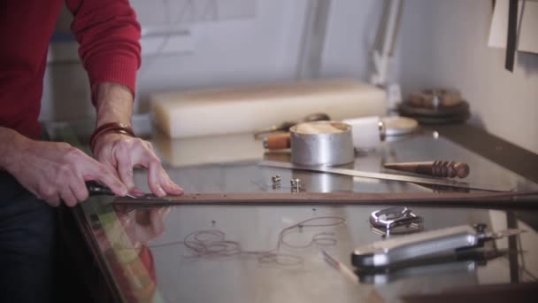 The tailor cuts off the piece of leather belt by the table using a sharp instrument — Stock Video