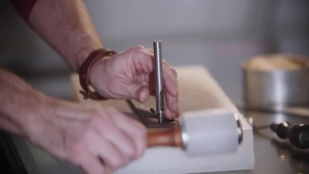 Мужчина выбрасывает маленькие дырочки в заготовку кожаного ремня инструментами — стоковое видео