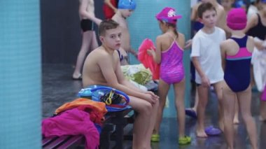 25-15-2021 RUSSIA, KAZAN - YÜKSEK KOMPETİONS - Yalnız çocuk bir bankta oturur ve diğer çocuklar havuz başında durur.