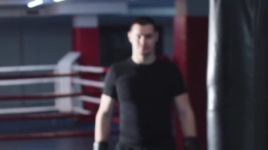 Çekici genç boksör kameraya doğru yürür ve ellerini eldivenlerle gösterir.