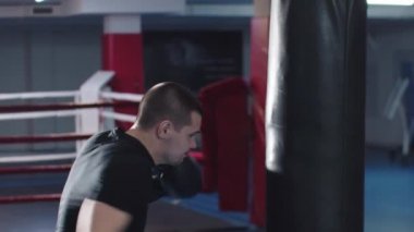 Çekici genç boksör kum torbasını yumrukluyor sonra kameraya bakıyor.