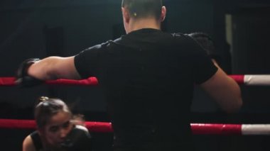 Genç kadın boks ringinde erkek antrenörüyle antrenman yapıyor.