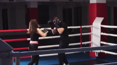 Genç bir kadın boks antrenmanı yapıyor. Kişisel koçuyla ringde.