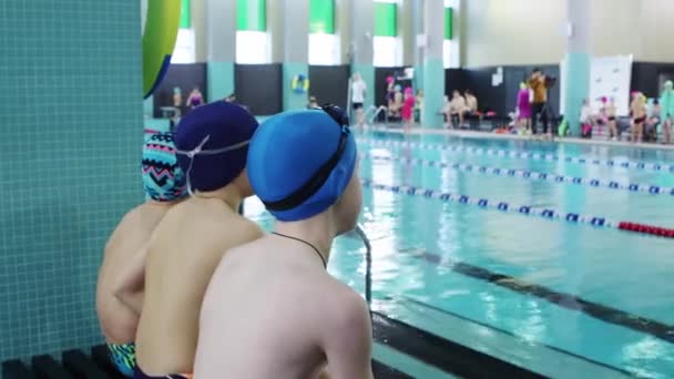 25-15-2021 RUSIA, KAZAN - COMPETICIONES DE Nadar - niños pequeños sentados en el banco junto a la piscina — Vídeos de Stock