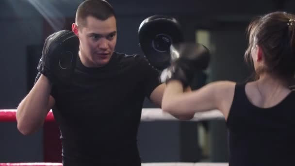 Mujer joven con pelo largo entrenamiento boxeo con su entrenador masculino personal en el anillo — Vídeos de Stock