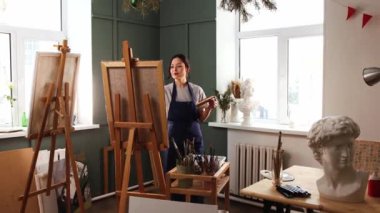 Sanat stüdyosu - genç kadın bir tabloyu sehpaya koyar - bir palet alır ve resim yapmaya başlar