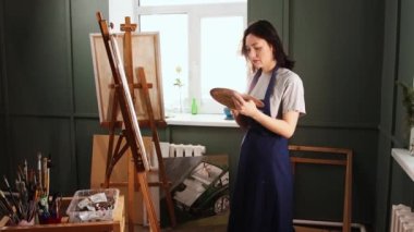 Sanat stüdyosu - palette renkleri karıştıran ve saçını bağlayan genç bir kadın