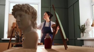 Sanat stüdyosu - mutlu genç kadın bir resim çiziyor - ön planda mermer büst heykel