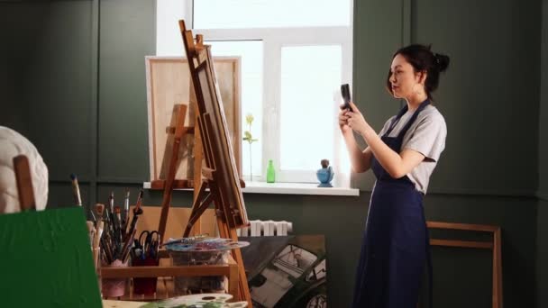 Studio d'arte - giovane donna fotografa il suo dipinto sul suo telefono — Video Stock