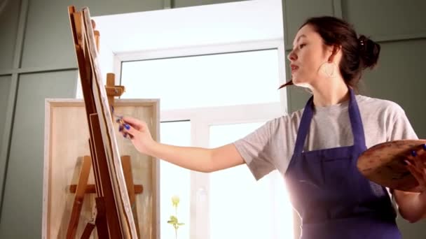 Estudio de arte - mujer joven dibujando una pintura sobre lienzo usando un cuchillo de paleta — Vídeos de Stock