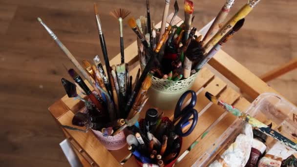Atelier d'art - bocaux remplis de pinceaux et jeune femme artiste dessin d'une peinture — Video