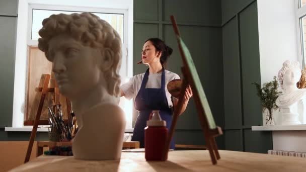 アートスタジオ-絵を描く幸せな若い女性-前景に大理石のバスト彫刻 — ストック動画