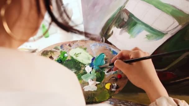 アートスタジオ-白いシャツの若い女性が色を混ぜ、絵を描く — ストック動画