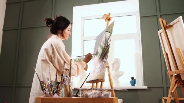Estudio de arte - mujer inspirada en la camisa blanca manchada cambiando pinceles y dibujando una pintura — Vídeos de Stock