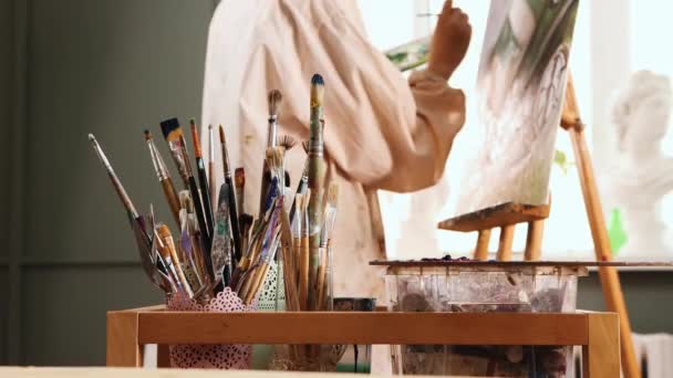Estudio de arte mujer artista en color camisa manchada cambio de pinceles y dibujo de una pintura — Vídeo de stock
