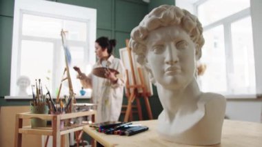 Şövalenin yanında duran bir kadın ressam - ön planda mermer büstü