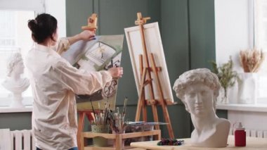 Bir kadın ressam, resim sehpasına yarım kalmış bir resim koyar ve çizmeye devam eder.