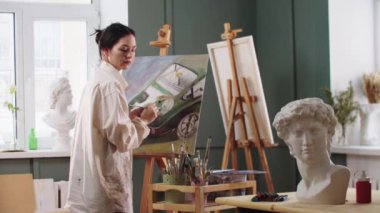 Sanat stüdyosundaki tuvale araba boyayan bir kadın sanatçı.