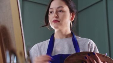 Güzel kadın ressam tuvale resim çiziyor ve fırçaları değiştiriyor.