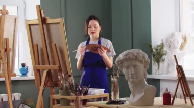Güzel ve güler yüzlü bir kadın sanat stüdyosunda bir tabloyla çalışıyor.