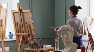 Güzel kadın sanatçı sanat stüdyosunda elini kameraya sallıyor.