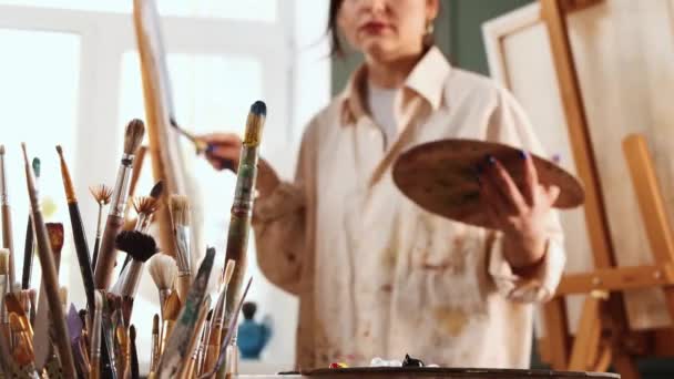 Art studio - woman artist drawing a painting on canvas and changing brushes — Stock Video