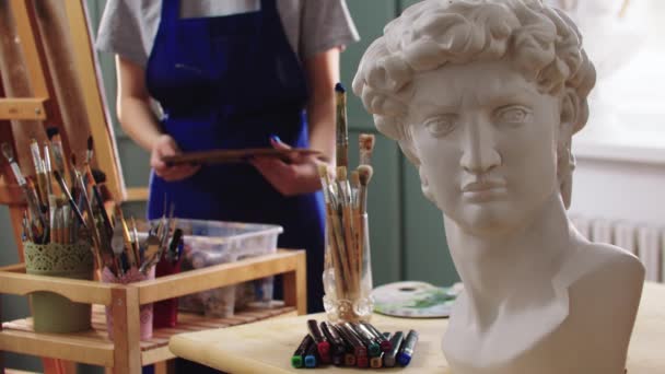 Жінка-художник вибирає пензлі з баночки - мармурова скульптура бюста на передньому плані — стокове відео