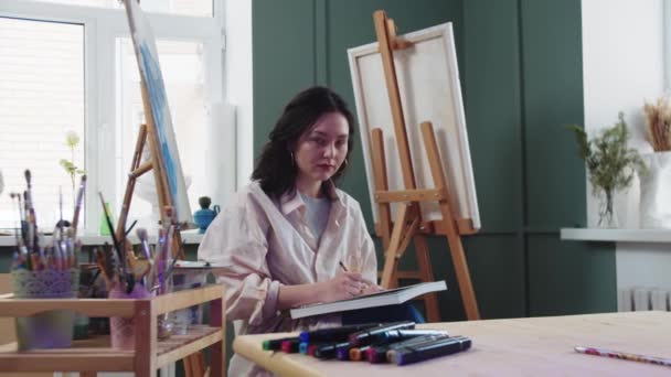 Een vrouwelijke kunstenaar schetst in een atelier — Stockvideo
