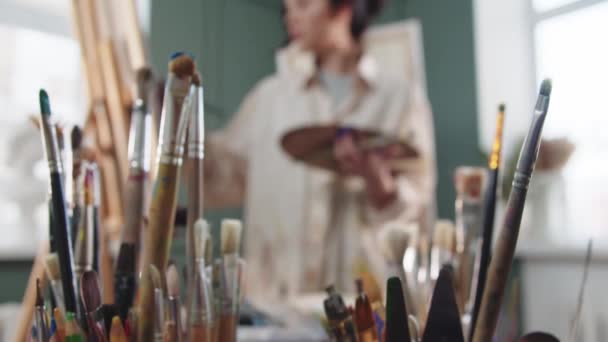 Γυναίκα καλλιτέχνης ζωγραφική στο στούντιο - παίρνει ένα πινέλο από το βάζο — Αρχείο Βίντεο