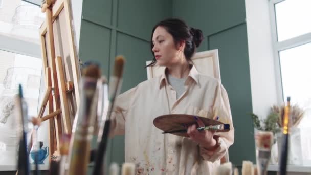 Une femme artiste peignant en atelier - pinceaux au premier plan — Video