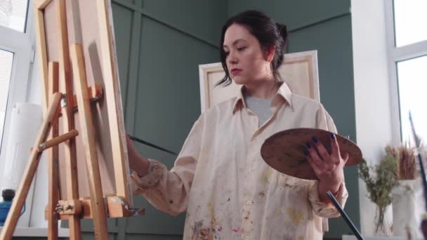 Una artista con una camisa manchada de pintura en el estudio — Vídeos de Stock