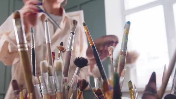 Uma artista mulher em uma camisa manchada de tinta muda um pincel — Vídeo de Stock