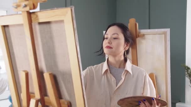 Une femme artiste dans une chemise tachée de peinture dessin sur toile — Video