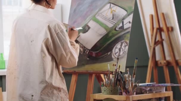 Une femme artiste peignant une voiture sur la toile sur chevalet dans un atelier d'art — Video