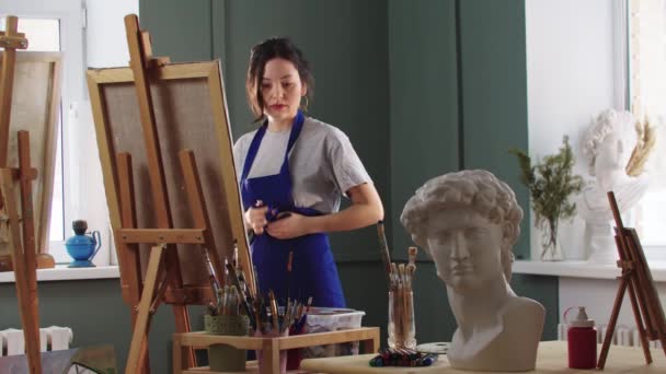 Una donna artista lega un grembiule su se stessa e inizia a dipingere su tela — Video Stock