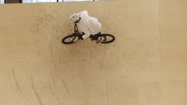Молодий чоловік катається на велосипеді BMX на фанерних гонках на тренувальному майданчику в приміщенні — стокове відео