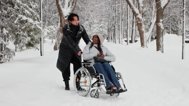 Νεαρός Ασιάτης και η μαύρη φίλη του στην αναπηρική καρέκλα μιλάνε στο χιονισμένο μονοπάτι — Αρχείο Βίντεο