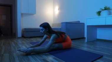 Evde mavi ışıkta spor yapmak - genç bir kadın ayaklarına kadar uzanıyor