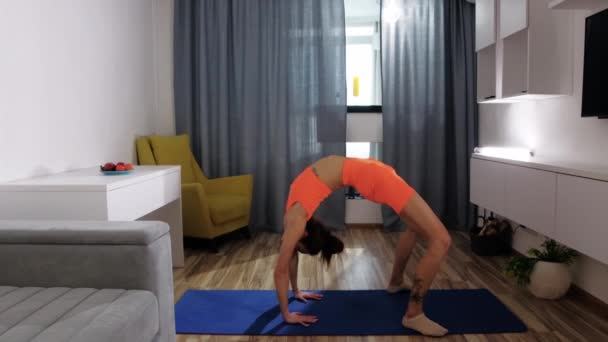 Fitness at home - a young woman leans back and stands on the bridge — Stock Video