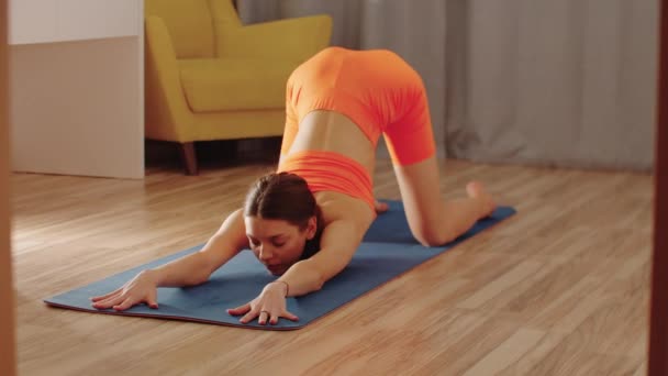 Joven mujer bonita en ropa naranja estirando su espalda en la esterilla de yoga — Vídeo de stock