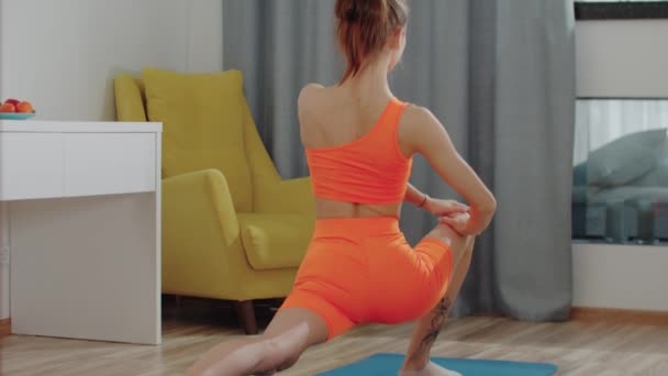 Mujer joven en traje deportivo naranja estirando su pierna — Vídeos de Stock