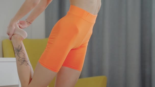 Ung smal kvinna i orange sportdräkt sträcker på benet — Stockvideo