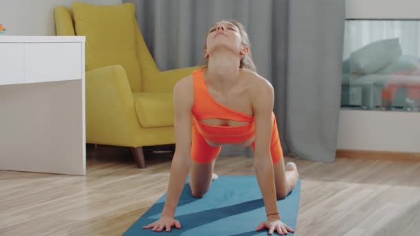 Mujer bonita joven en traje deportivo naranja haciendo ejercicio en la esterilla de yoga — Vídeo de stock