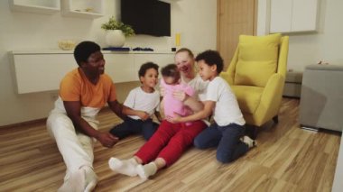 Siyah baba ve beyaz anne yerde çocuklarıyla oynuyorlar.